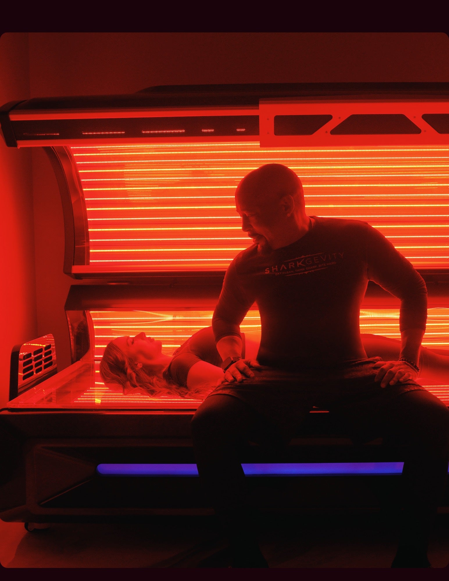 Two people beside and reclining in an open red light therapy bed